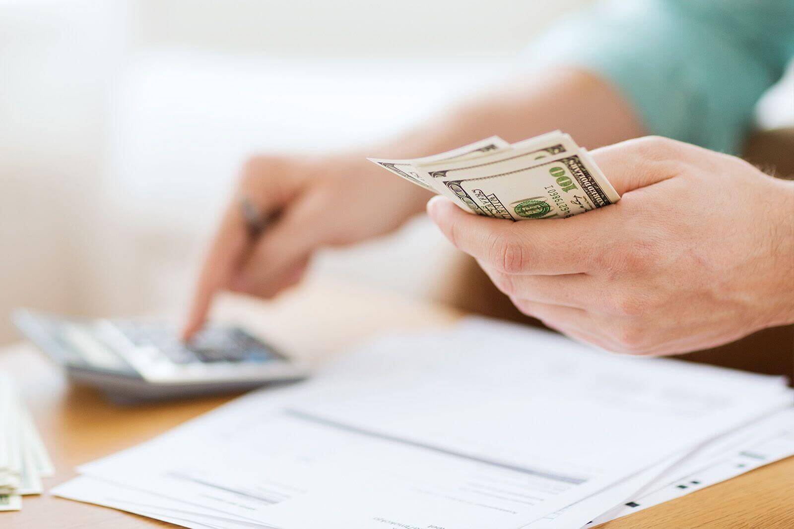 One hand with money in it and another with a calculator