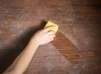 A person wiping a wooden surface with a sponge, removing a layer of dust